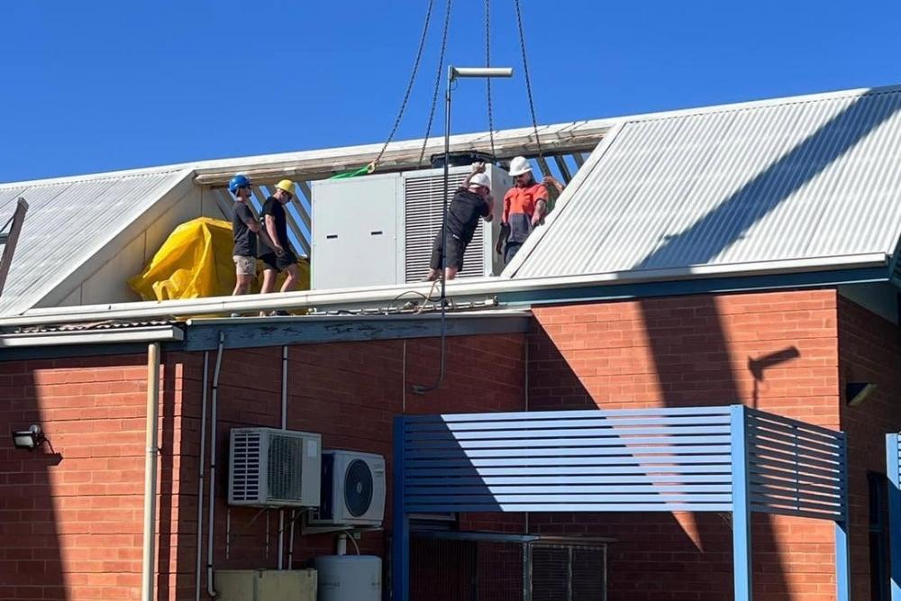 Technicians positioning a large HVAC unit hoisted by crane